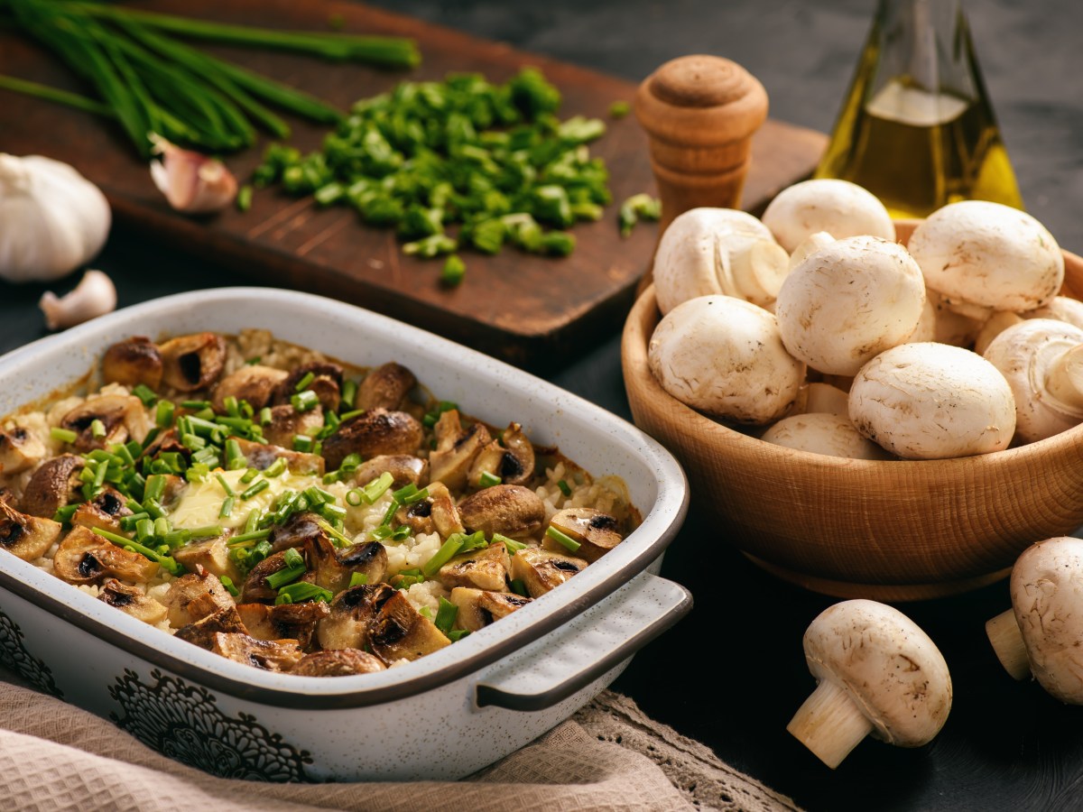 Reisauflauf mit Pilzen in Auflaufform, daneben eine Schale mit Champignons und KrÃ¤uter.