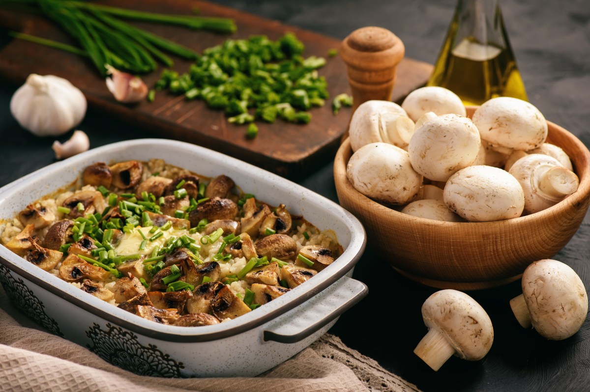 Reisauflauf mit Pilzen in Auflaufform, daneben eine Schale mit Champignons und KrÃ¤uter.