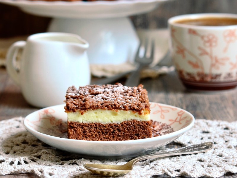 Ein StÃ¼ck Schoko-Streuselkuchen, daneben eine Tasse Kaffee, ein KÃ¤nnchen Milch und der restliche Kuchen.