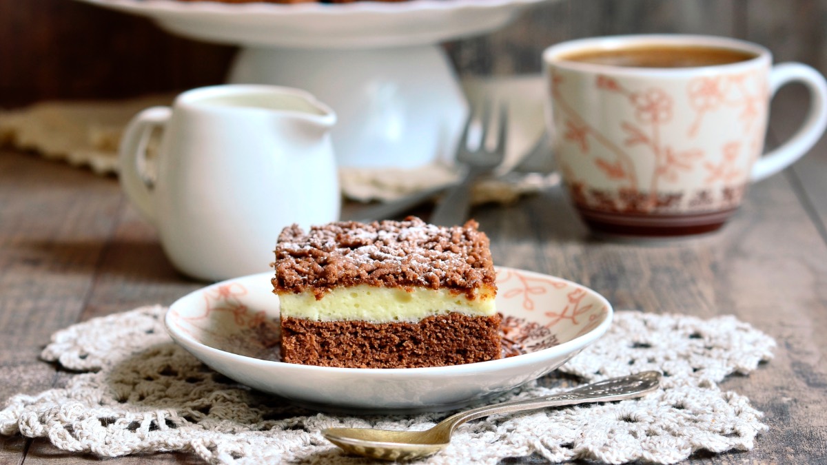 Ein StÃ¼ck Schoko-Streuselkuchen, daneben eine Tasse Kaffee, ein KÃ¤nnchen Milch und der restliche Kuchen.