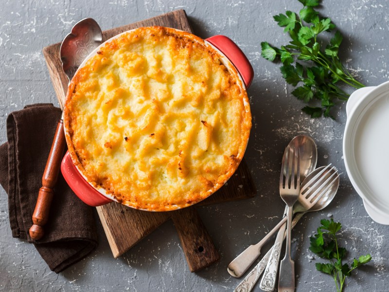 Shepherd's Pie mit Linsen und KartoffelpÃ¼ree in runder Auflaufform in der Draufsicht, daneben Besteck und KrÃ¤uter.