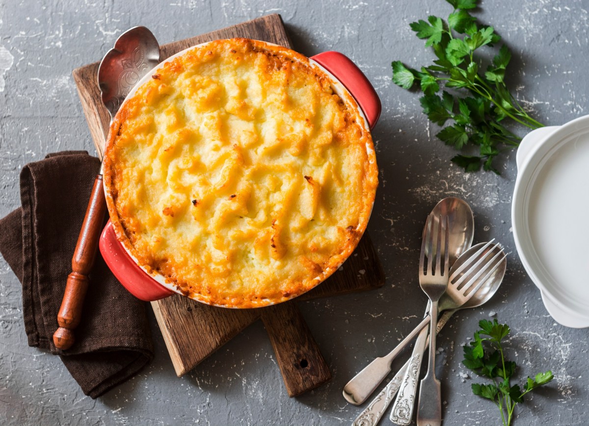 Shepherd's Pie mit Linsen und KartoffelpÃ¼ree in runder Auflaufform in der Draufsicht, daneben Besteck und KrÃ¤uter.