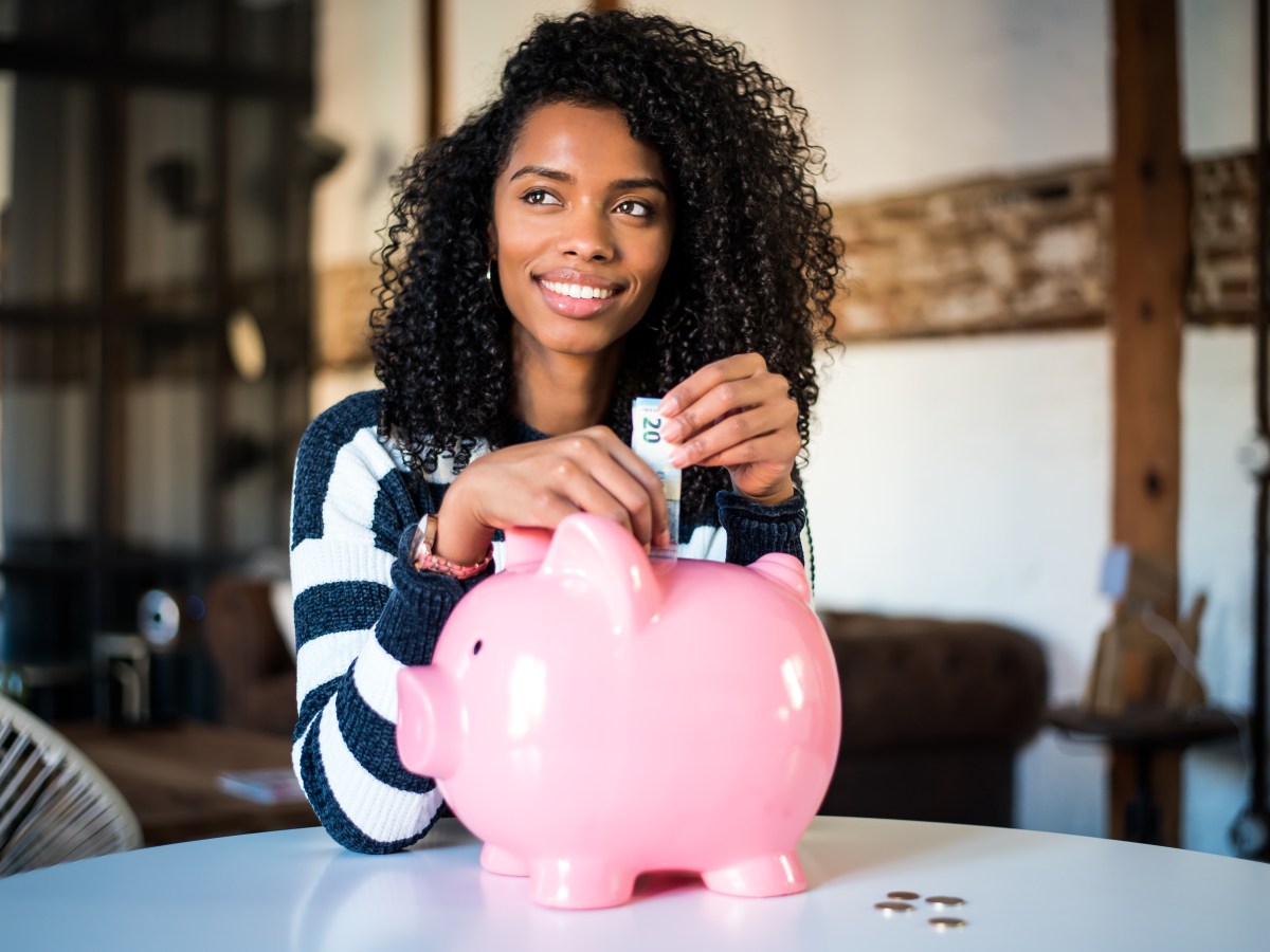 Schwarze Frau steckt einen 20-Euro Schein in ein Sparschwein.