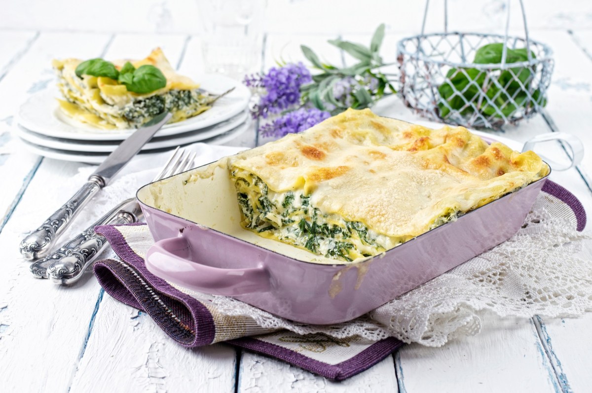 Spinat-Ricotta-Lasagne in einer Auflaufform, ein StÃ¼ck bereits herausgenommen und auf einem Teller im Hintergrund.