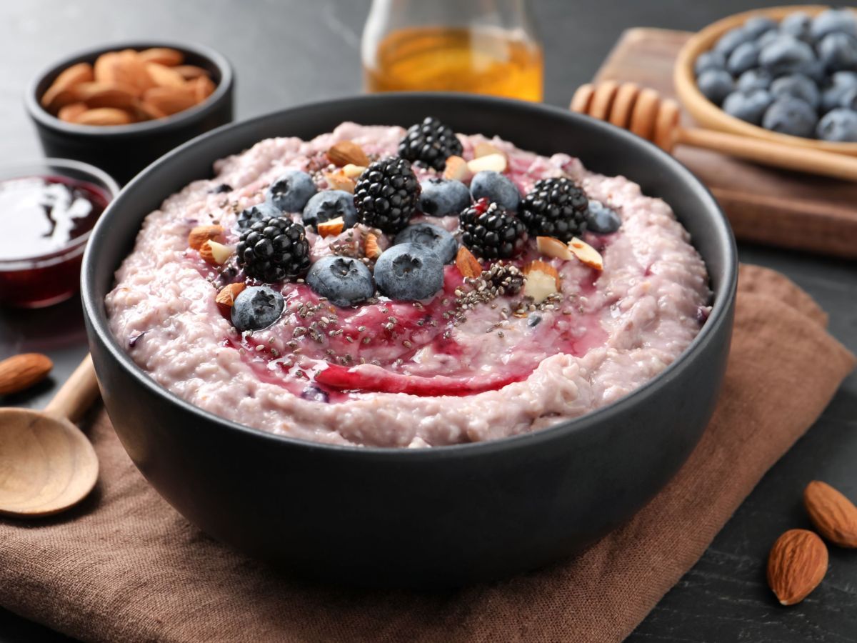 SÃ¼ÃŸer Couscous, serviert in einer dunklen Schale. Frische Heidelbeeren liegen als Deko obenauf. SchÃ¤lchen mit Beeren, Honig und Mandeln stehen als Deko auÃŸen herum.