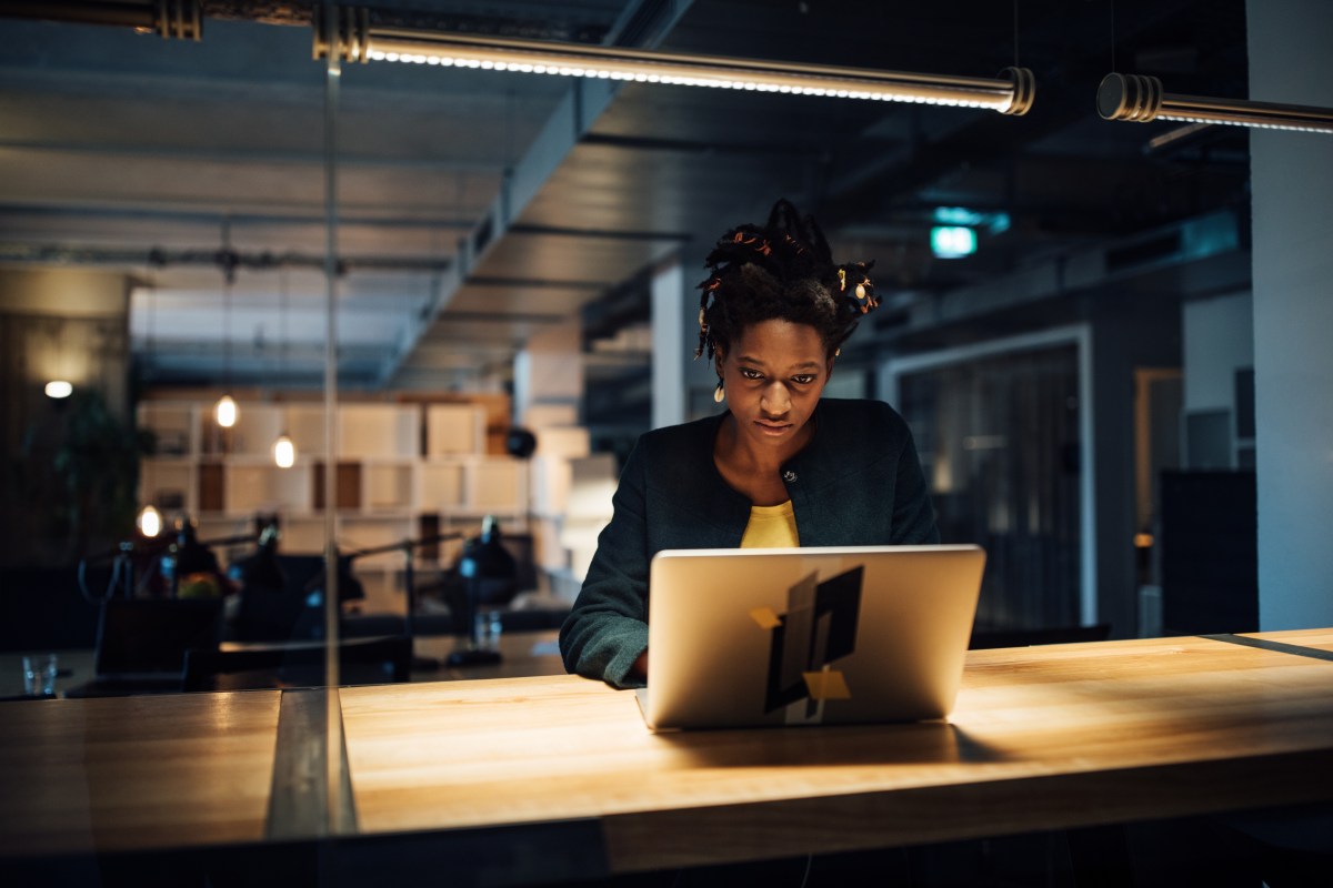 Geschäftsfrau arbeitet spät am Laptop, während sie im Büro am Schreibtisch sitzt