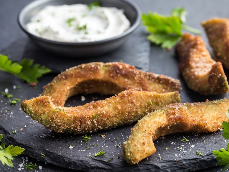 Frittierte Avocado auf schwarzem Teller mit KrÃ¤uter-Dip.