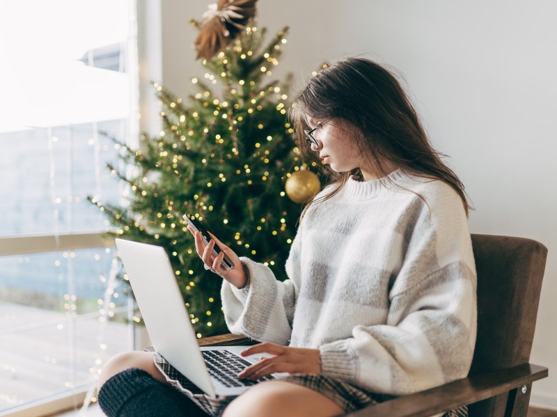 Junge Frau arbeitet an einem Laptop-Computer. Im Hintergrund steht ein Weihnachtsbaum.