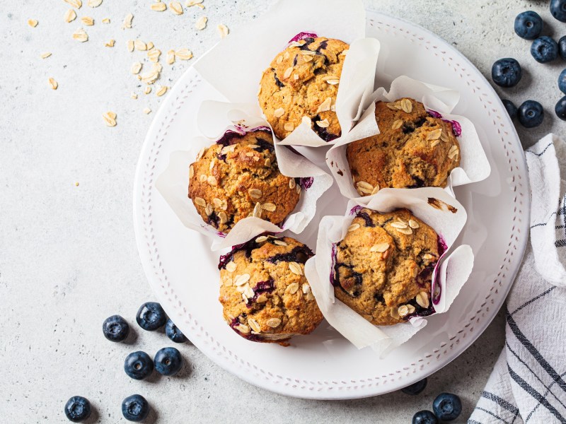 Teller mit Haferflocken-Muffins mit Blaubeeren auf hellem Untergrund