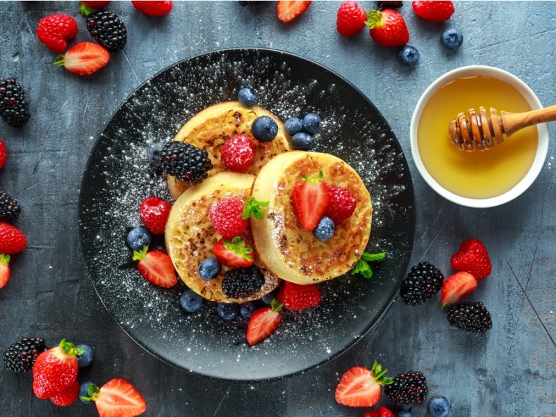 Englische Crumpets auf einem schwarzen Teller und Obst.