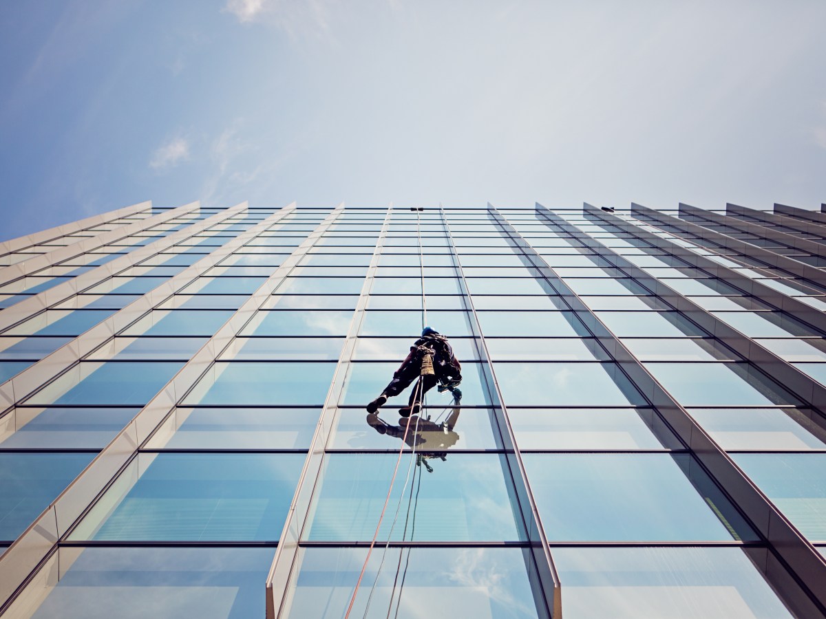 Eine Person reinigt die Fenster eines Hochhauses.