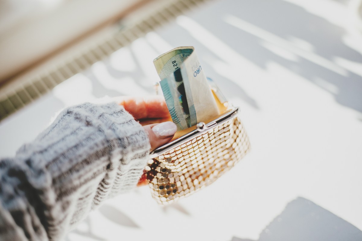 Die weibliche Hand hÃ¤lt eine goldene Handtasche mit Euro-Scheinen.