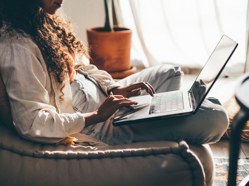 Junge Frau mit Laptop arbeitet im Wohnzimmer.