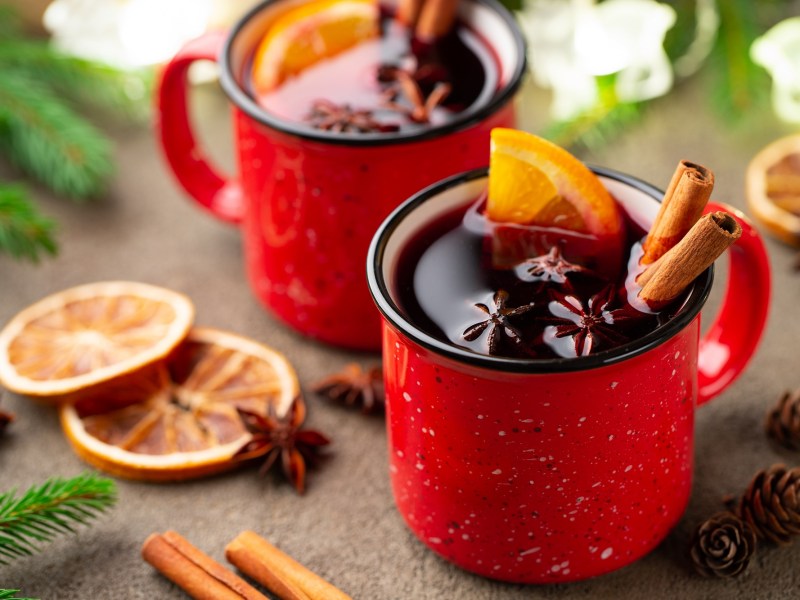 2 rote Tasse mit GlÃ¼hwein, der mit GlÃ¼hweingewÃ¼rzen wie Zimt und Anis sowie Orangenscheiben garniert ist.