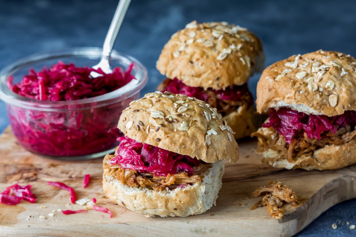 3 kleine Rotkohl-GÃ¤nse-Burger auf einem Brett, auf dem auch eine GlasschÃ¼ssel mit Rotkohl steht.