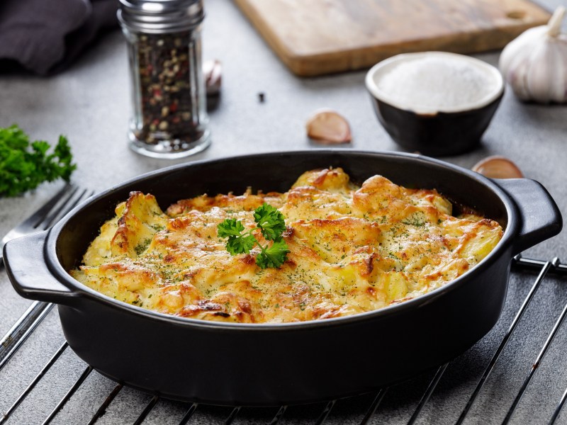 Knoblauch-Kartoffelauflauf in einer dunken ovalen Auflaufform, die auf einem Ofengitter steht.