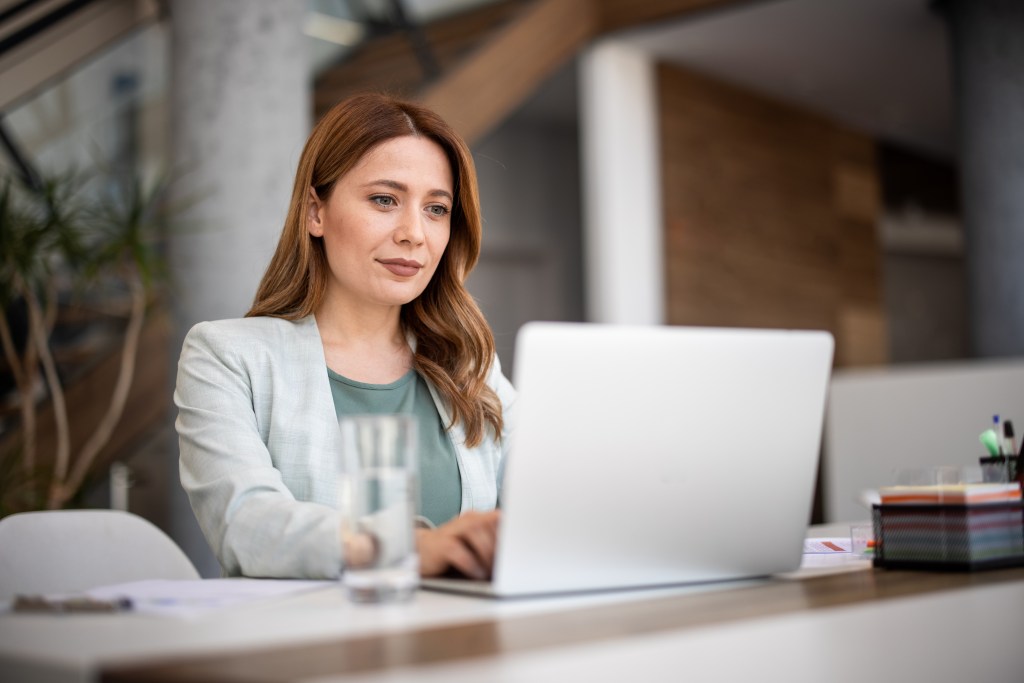 Frau mit braunen Haaren sitzt am laptop und arbeitet.