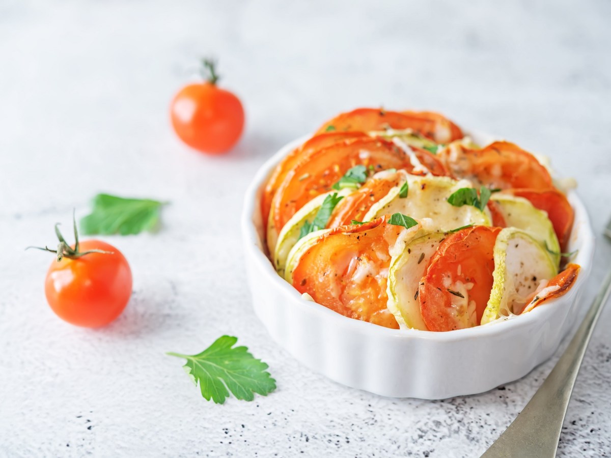 Mini-GemÃ¼se-Gratin mit Tomate und Zucchini in einer weiÃŸen runden Auflaufform, daneben Mini-Tomaten.