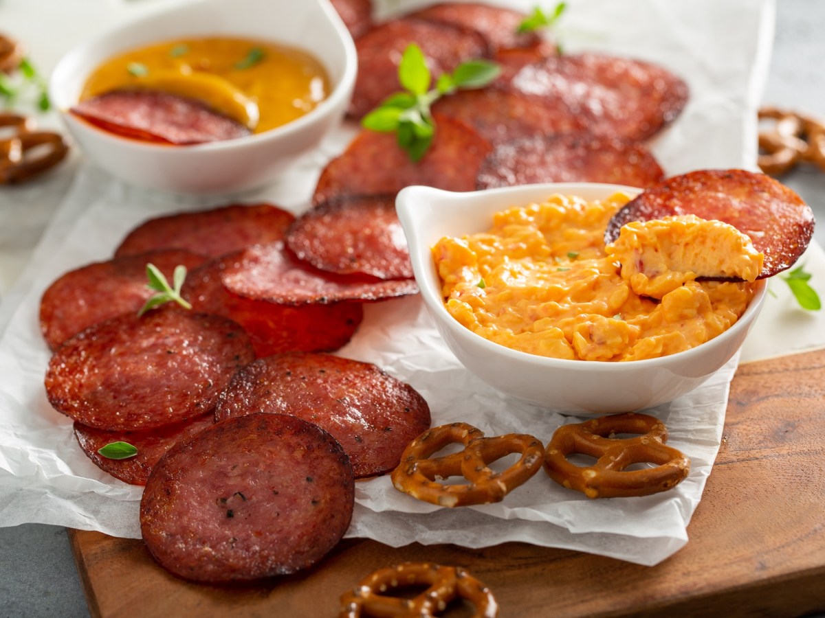 Salami-Chips mit KÃ¤sedip auf einer Serviette. Daneben liegen Salzbrezeln.