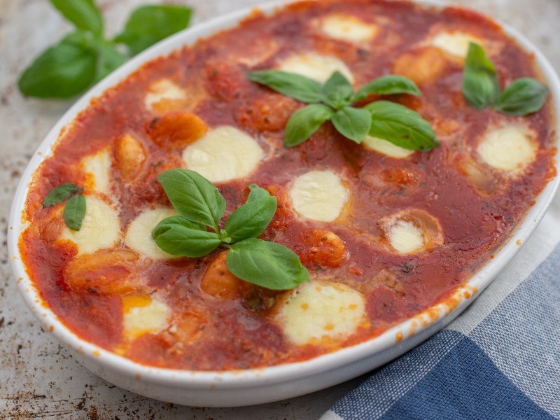 Gnocchi alla sorrentina: Ã¼berbackene Gnocchi mit TomatensoÃŸe und Mozzarella in einer Auflaufform, garniert mit Basilikum.