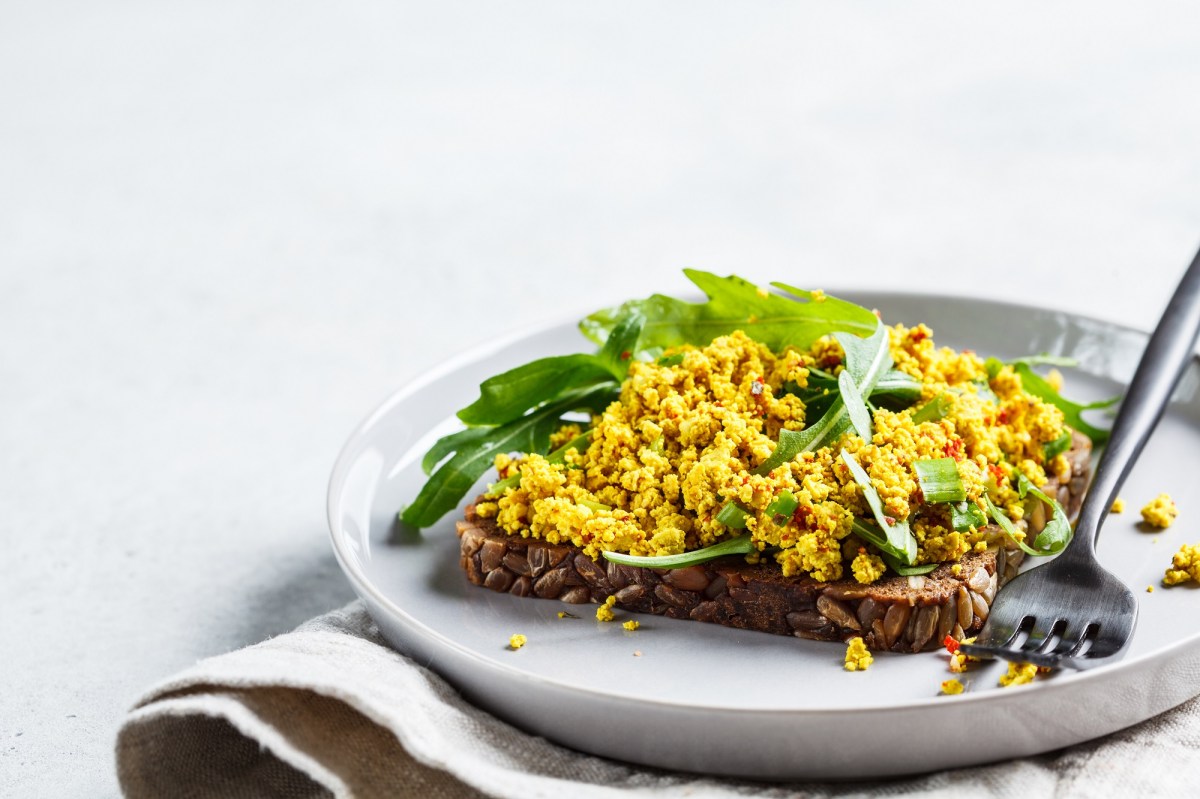 Ein Brot belegt mit veganem RÃ¼hrei und Rucola auf einem Teller, Nahaufnahme.