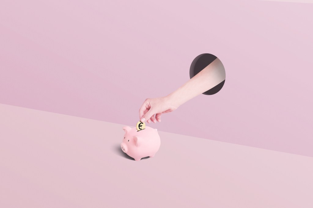 Hand legt eine goldene Euro-Münze in ein rosa Sparschwein.