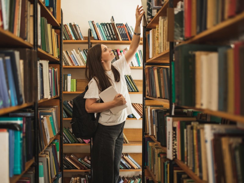 Studentin steht in der UniversitÃ¤tsbibliothek und sucht ein Buch.