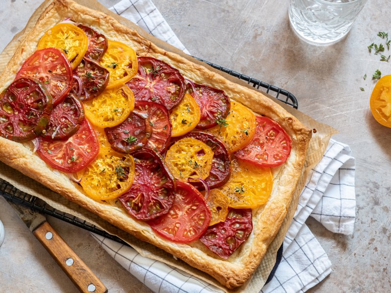 BlÃ¤tterteig-Tarte mit Tomaten auf einem Kuchengitter, das auf einem Geschirrtuch liegt.