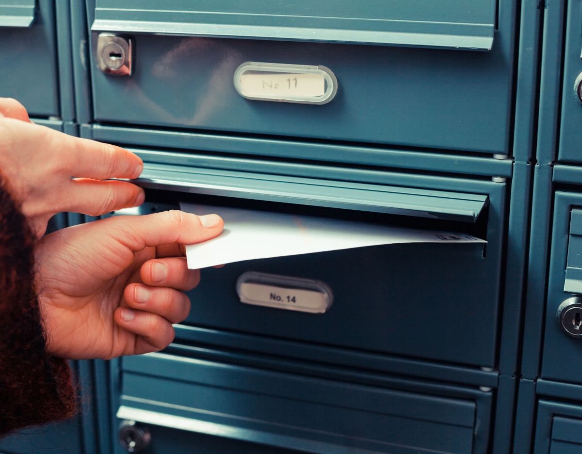 Eine Frau zieht einen Brief aus dem Briefkasten.