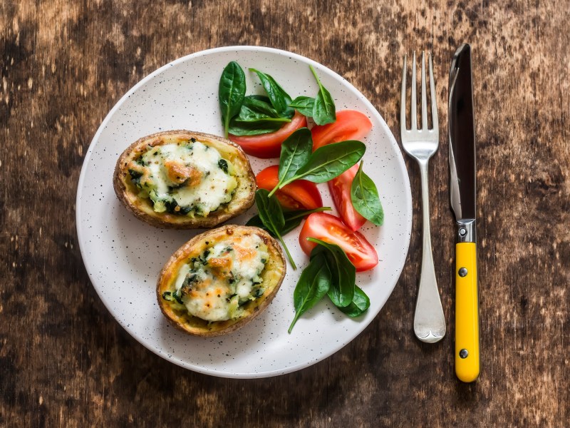 2 Bruschetta-Kartoffeln auf einem Teller, daneben ein kleiner Salat, neben dem Teller Messer und Gabel, Draufsicht.