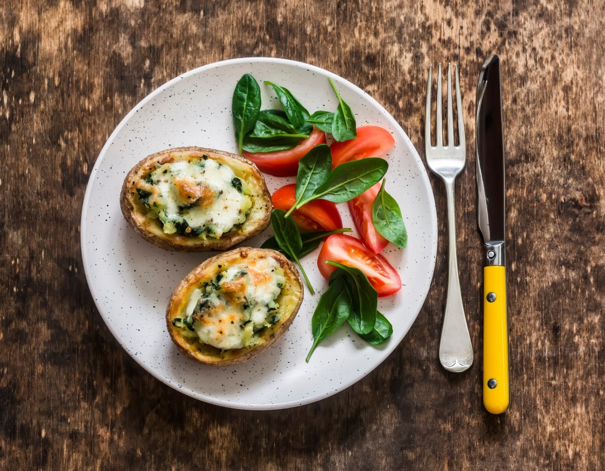 2 Bruschetta-Kartoffeln auf einem Teller, daneben ein kleiner Salat, neben dem Teller Messer und Gabel, Draufsicht.