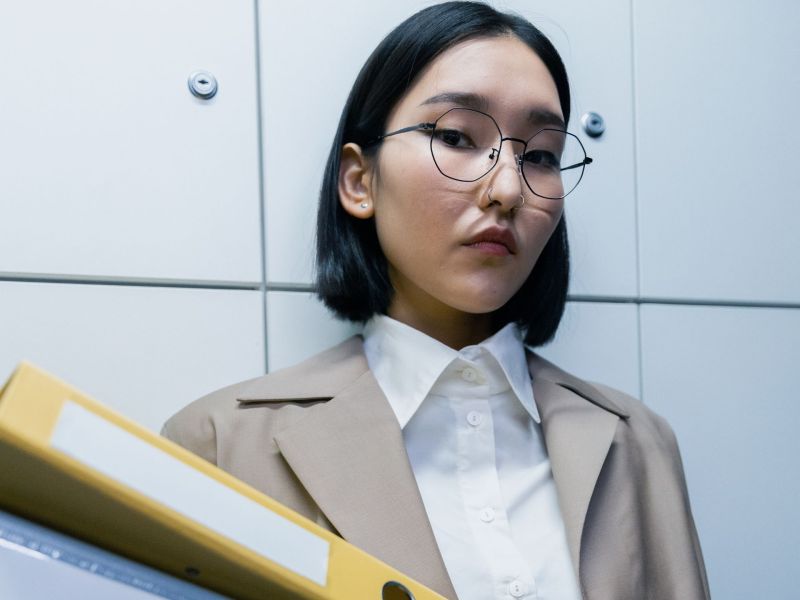 Eine Frau mit einem schwarzen Bob und Brille trägt einen gelben Aktenordner.