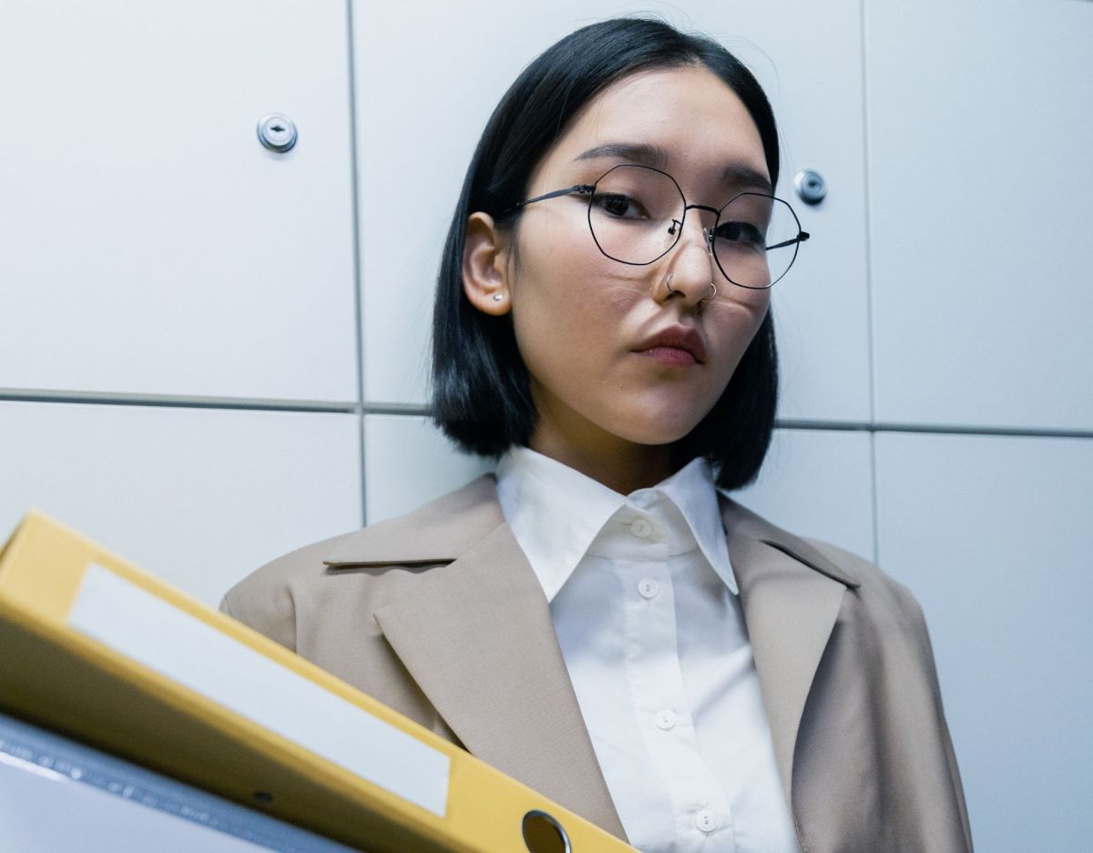 Eine Frau mit einem schwarzen Bob und Brille trÃ¤gt einen gelben Aktenordner.