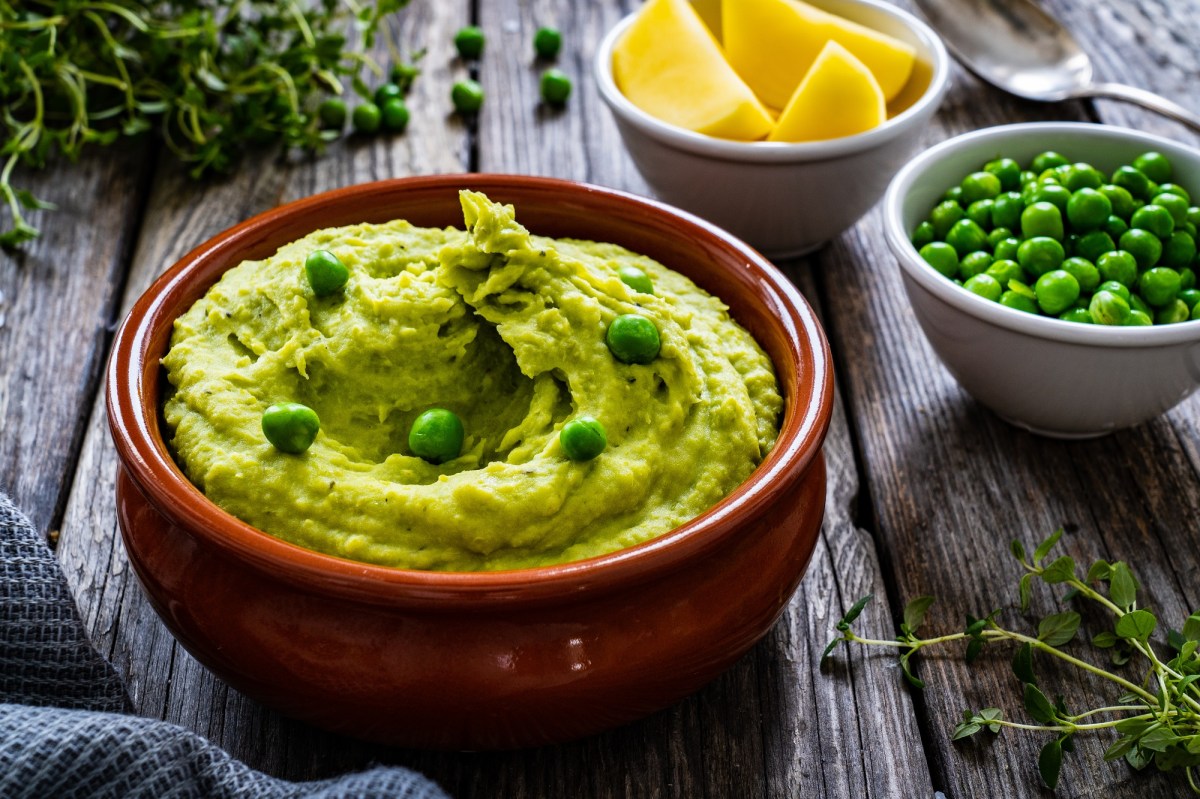 Eine braune Schale Erbsen-Guacamole, garniert mit ganzen Erbsen, daneben eine Schale Erbsen und eine Schale Zitronenspalten sowie KrÃ¤uter.