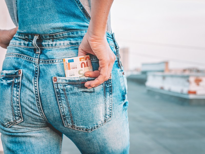 Die Hand einer Frau holt Euro-Scheine aus der Gesäßtasche ihrer Jeans.