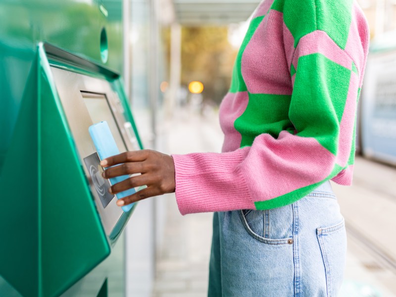 Frau in pink, grünen Pullover hebt Geld ab.