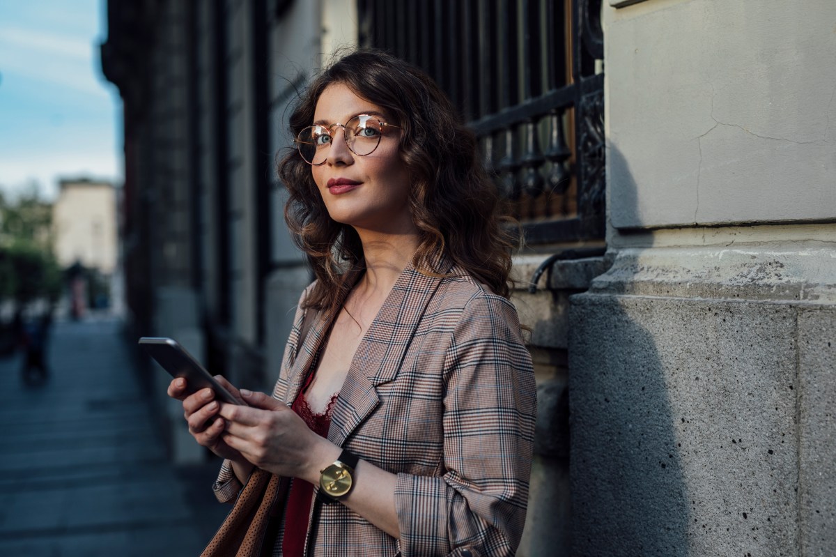 Eine elegante Frau steht auf der StraÃŸe und hÃ¤lt ihr Telefon in der Hand.