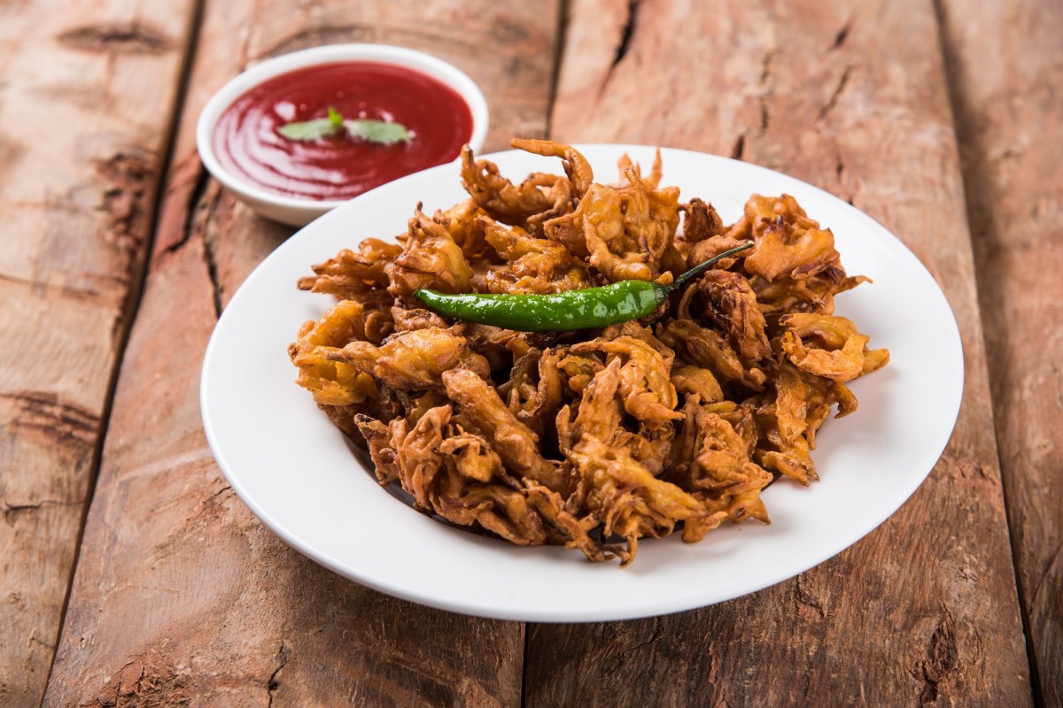 Indische GemÃ¼sekrapfen auf einem weiÃŸen Teller, dekoriert mit einer grÃ¼nen Chili und serviert mit einer roten SoÃŸe.