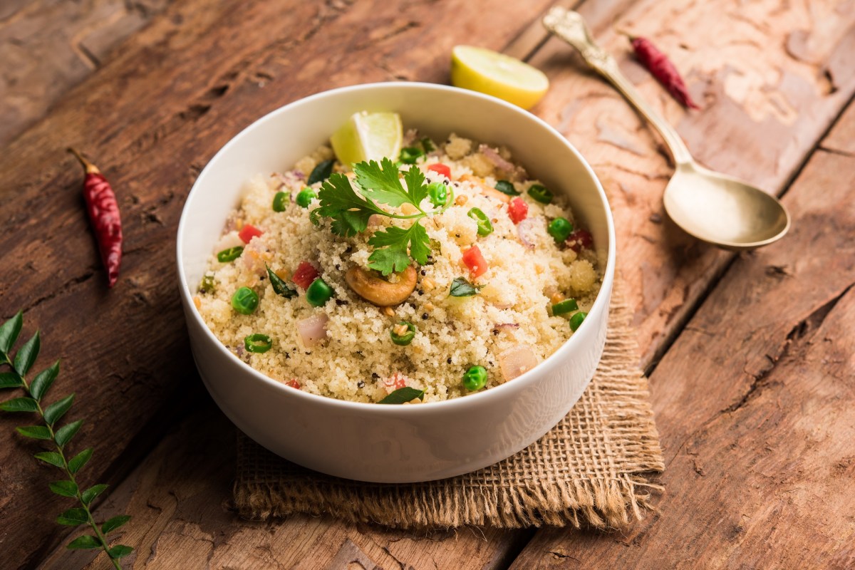 Eine Schale indisches Upma, HartweizengrieÃŸ, mit etwas GemÃ¼se und KrÃ¤utern, daneben ein LÃ¶ffel.