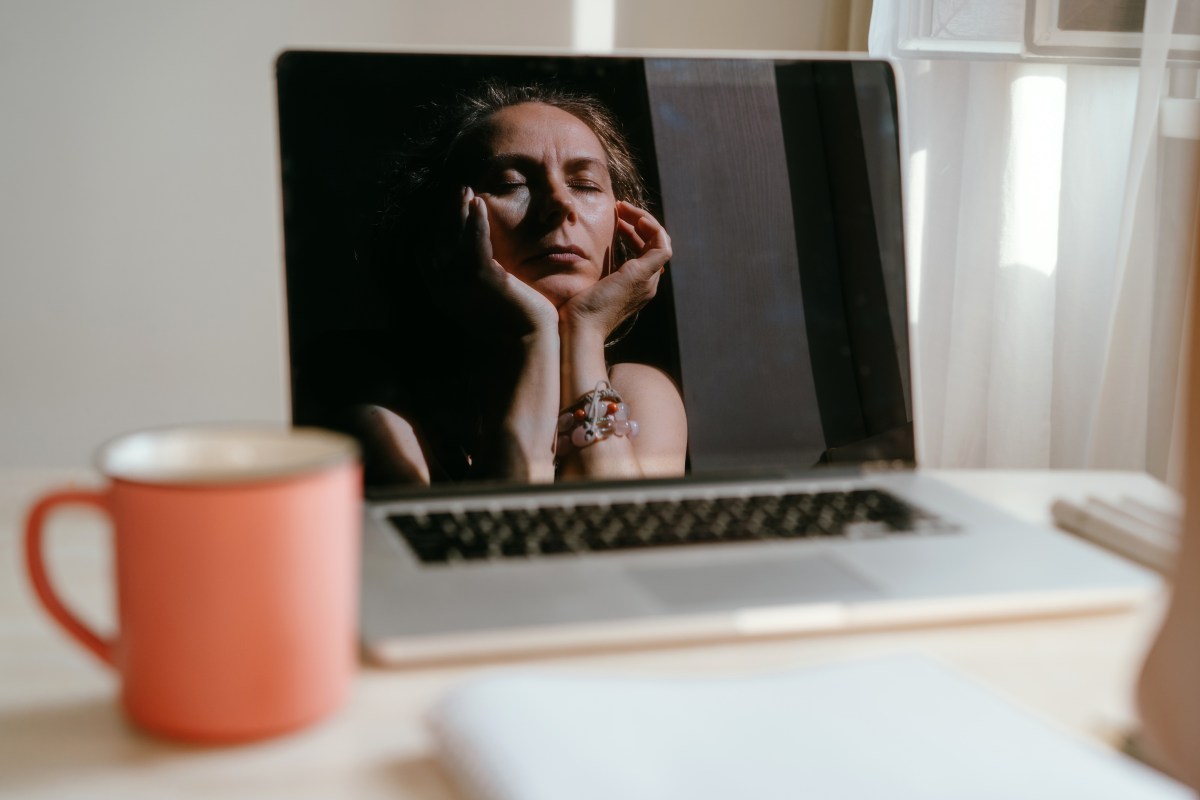 Porträt einer Frau, die am Schreibtisch sitz. Hier Spiegelbild spiegelt sich in ihrem Laptop.