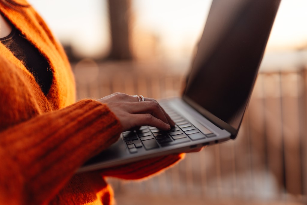 Frau tippt mit der Hand auf einer Laptop-Tastatur in einer Außenumgebung in der Stadt.