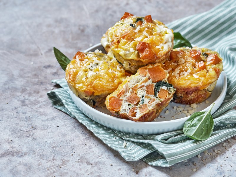 4 Kroketten-Muffins mit GemÃ¼se und Schmand auf einem Teller, der auf einem gestreiften Geschirrtuch steht.