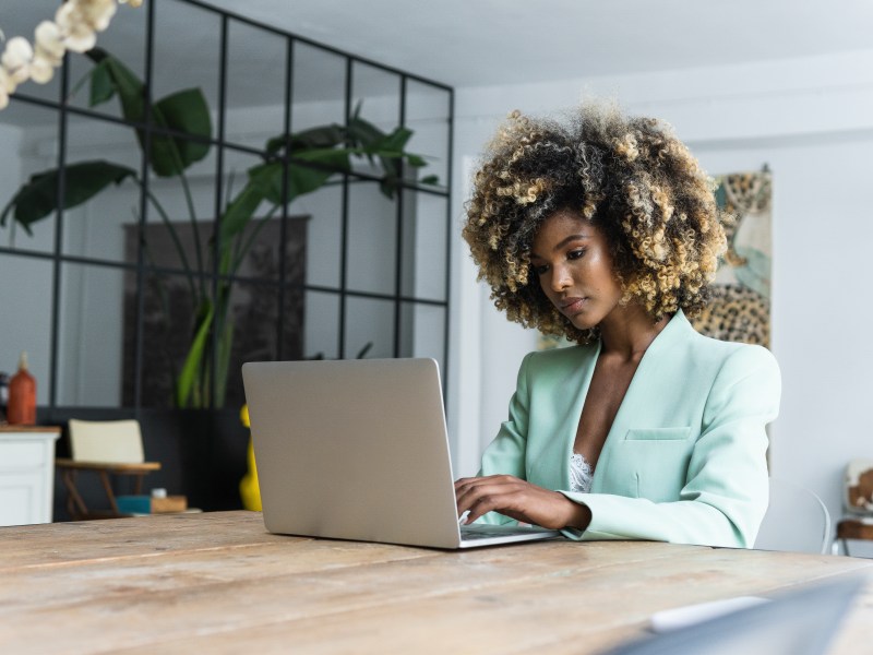 Eine Frau mit Afro sitzt an einem Tisch und arbeitet am Laptop.