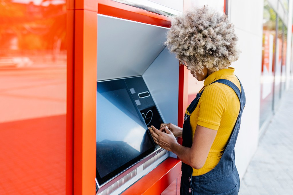 Frau mit Afro-Frisur am Geldautomaten.
