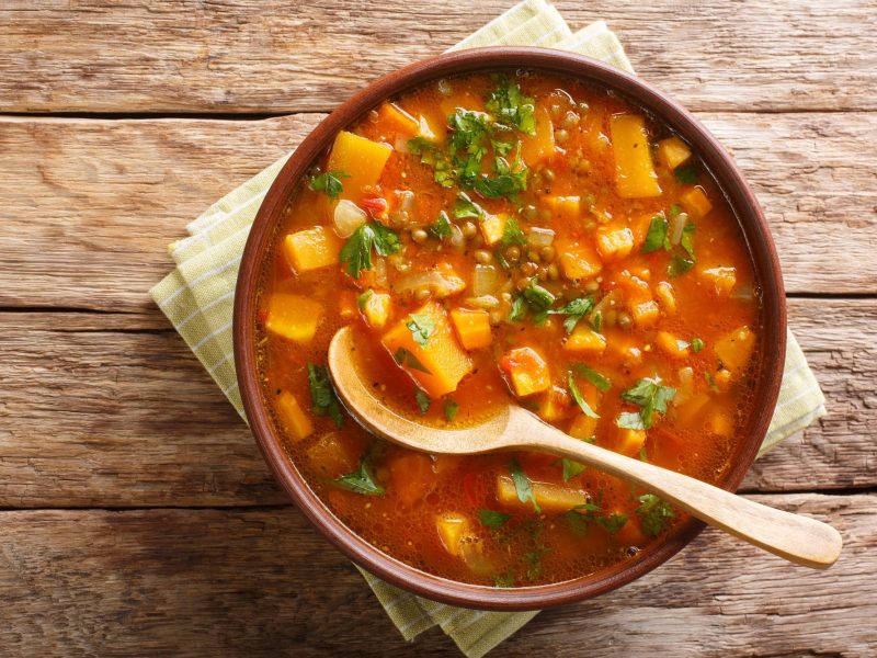 Eine SchÃ¼ssel SÃ¼ÃŸkartoffel-Curry-Suppe mit HolzlÃ¶ffel in der Draufsicht.