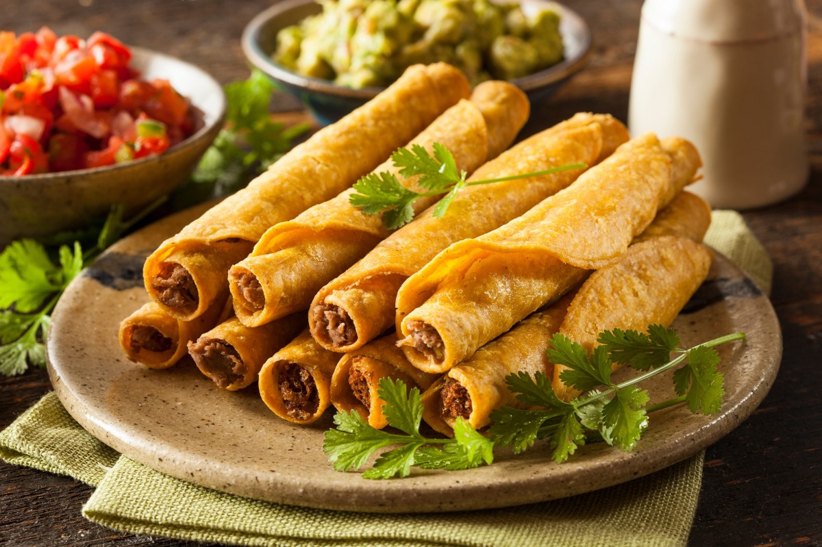 Taquitos mit HackfleischfÃ¼llung auf einem beigen Teller, garniert mit Koriander und serviert mit Tomaten-Salsa, Guacamole und Sour Cream.