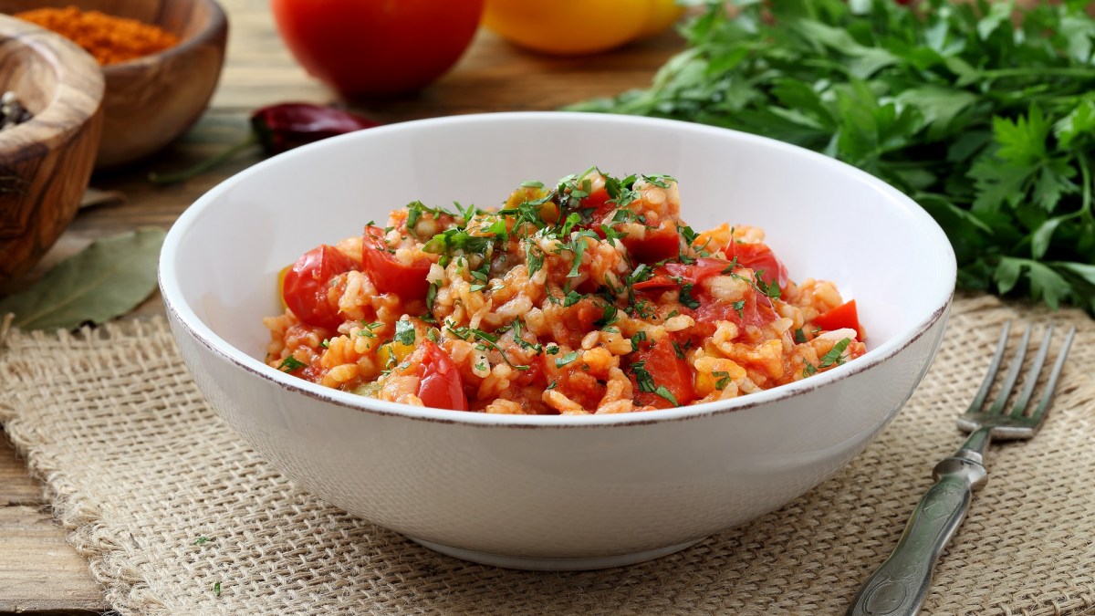 Eine SchÃ¼ssel Tomatenreis mit Spinat, dahinter frische Zutaten.