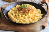 Eine gusseiserne Pfanne vegane KÃ¤sespÃ¤tzle mit RÃ¶stzwiebeln und Petersilie, Nahaufnahme.