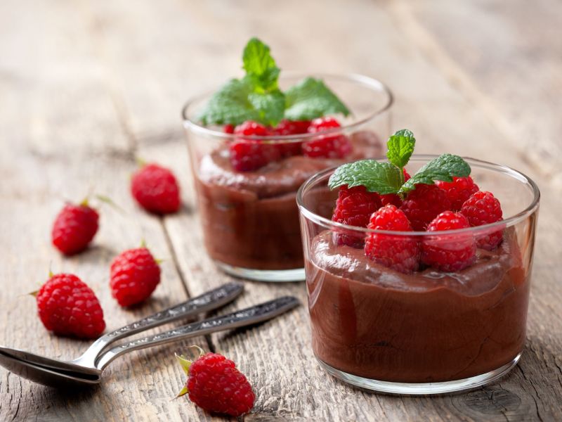 Vegane Mousse au Chocolat, serviert in zwei GlÃ¤sern. Himbeeren dienen als Deko in den GlÃ¤sern und daneben.