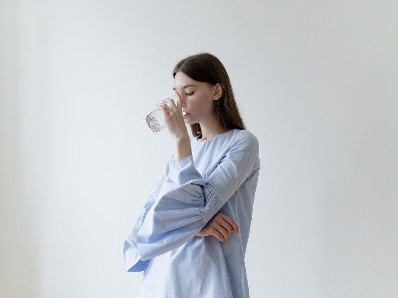 Eine Frau in einem blauen Hemd trinkt ein Glas Wasser.